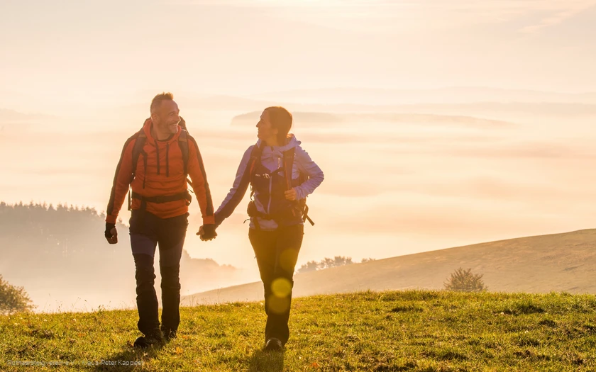 Zwei Rothaarsteig-Wanderer im Sonnenaufgang auf einer Wiese