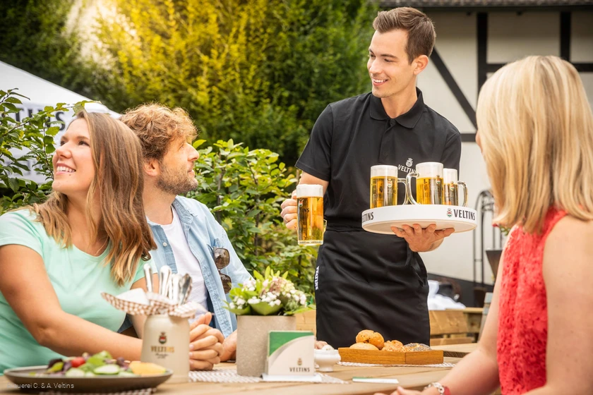 Een groep krijgt verse Veltins geserveerd aan de tafel buiten
